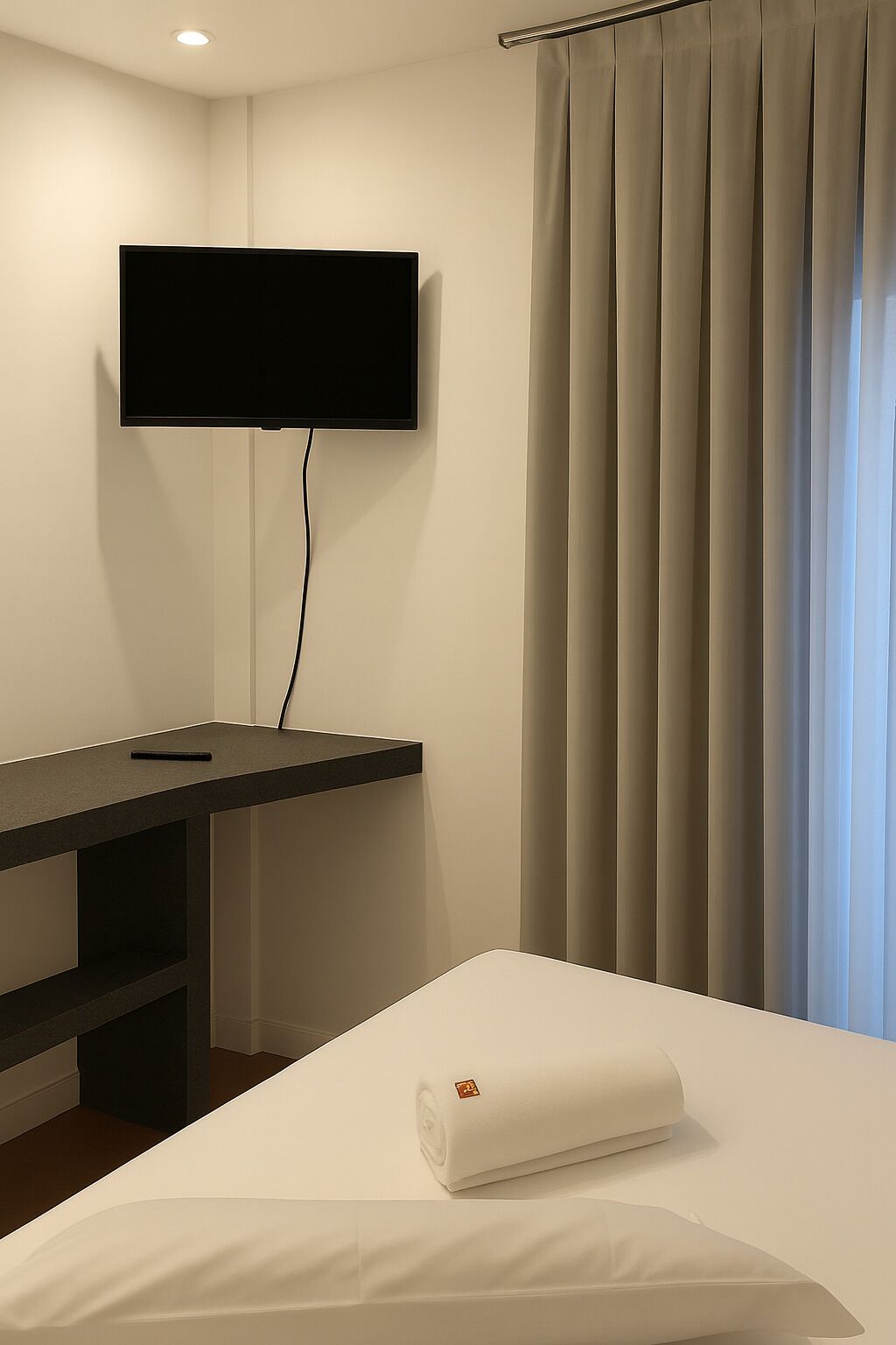 A hotel room with a bed, a desk, and a television mounted on the wall.