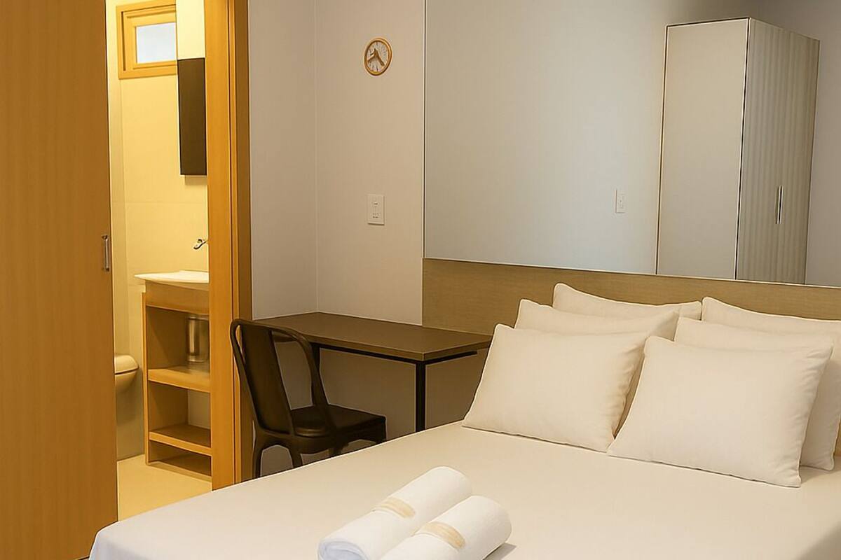 A hotel room with a bed, a desk, and a mirror.