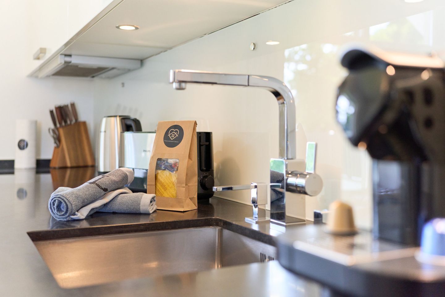 A modern kitchen with a stainless steel sink, a coffee machine, and a paper bag on the counter.