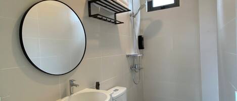 Une salle de bain moderne avec un lavabo, des toilettes et une douche, le tout de couleur blanche. On trouve un porte-serviettes au-dessus du lavabo et une petite fenêtre au-dessus de la douche.
