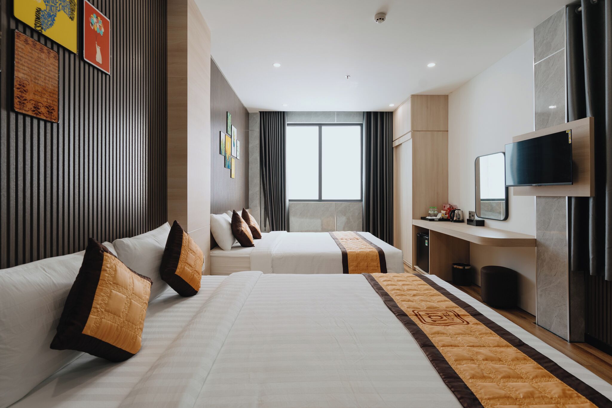 A hotel room with two beds, a TV, a desk, and a large window.