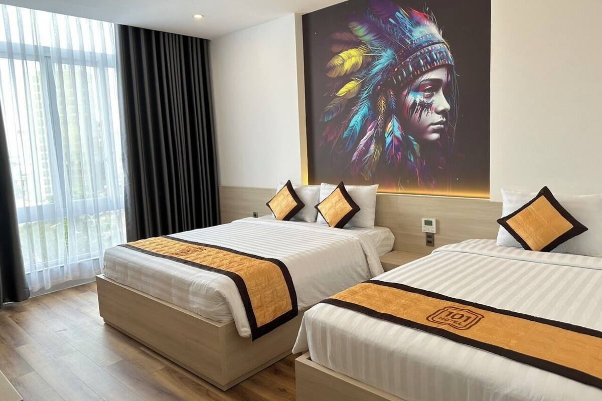 A hotel room with two beds, a large window with curtains, and a wall-mounted screen displaying a colorful image.