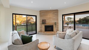 Amplia sala de estar con chimenea, dos sofás, una mesa de centro y puertas de cristal correderas que dan a un patio con piscina.