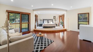 Un dormitorio amplio con una cama grande, una zona de estar con un sofá y una mesita, y vistas al exterior a través de grandes ventanales.