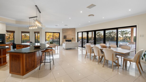 Una cocina amplia con una isla central, ventanas grandes y un comedor con sillas y una mesa.