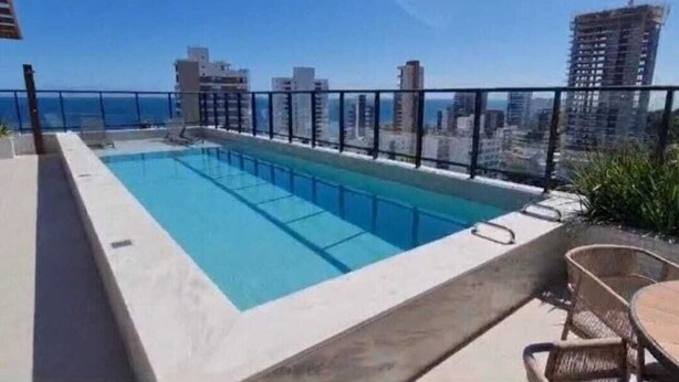 Une piscine sur le toit, offrant une vue sur la ville, entourée d’une rambarde et aménagée avec des chaises et des tables.