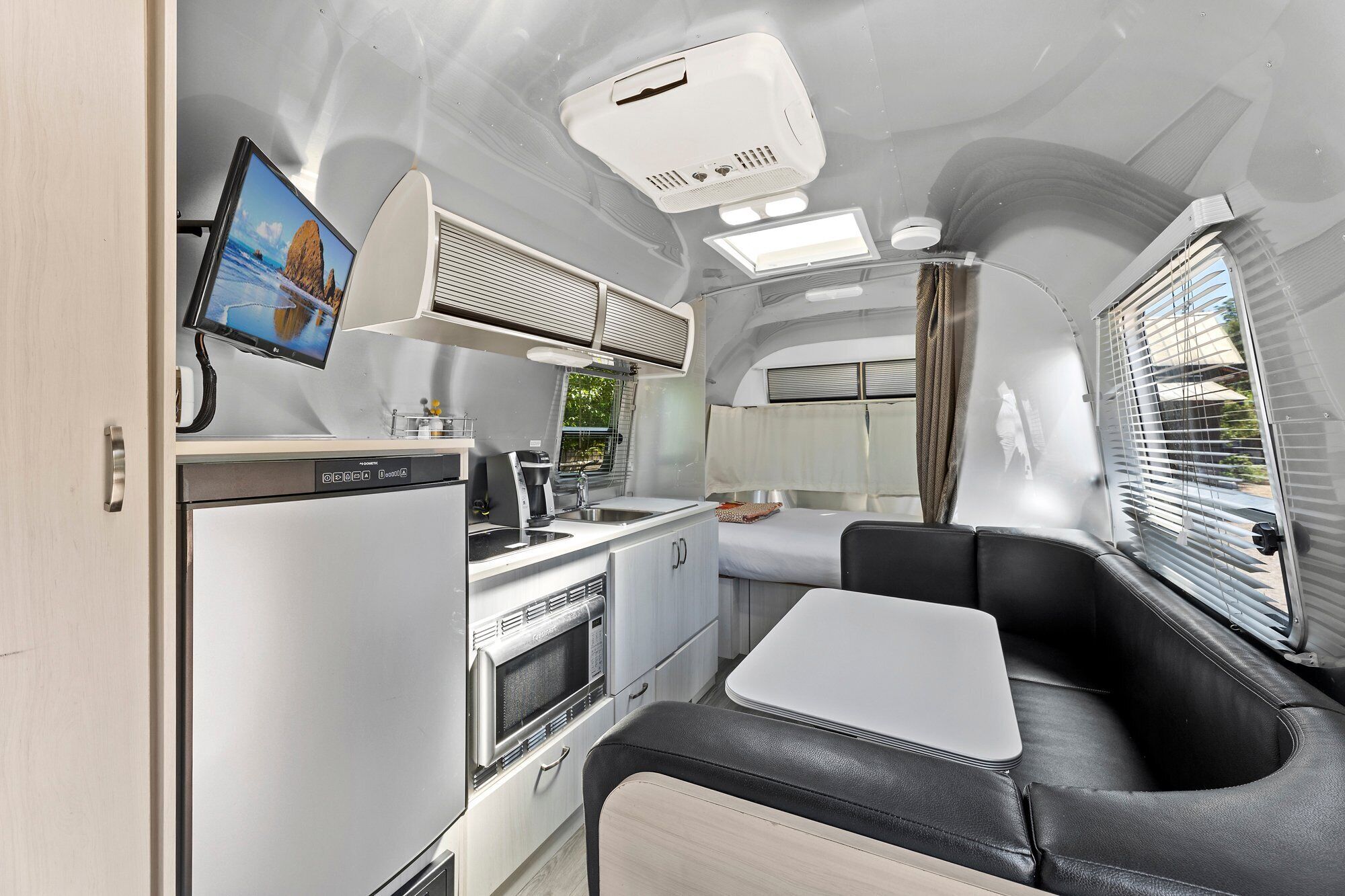 A compact kitchen with a microwave, stove, and sink, a small dining area with a table, and a window with blinds.