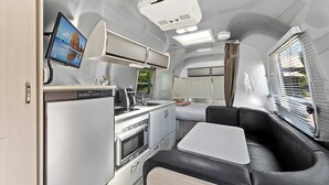 A compact kitchen with a microwave, stove, and sink, a small dining area with a table, and a window with blinds.