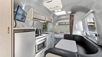 A compact kitchen with a microwave, stove, and sink, a small dining area with a table, and a window with blinds.