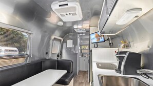 A compact RV interior with a kitchenette, seating area, and a TV screen.