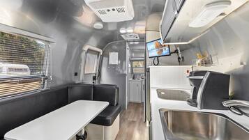A compact RV interior with a kitchenette, seating area, and a TV screen.