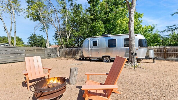 A campsite with two wooden chairs, a metal fire pit, and a vintage trailer.