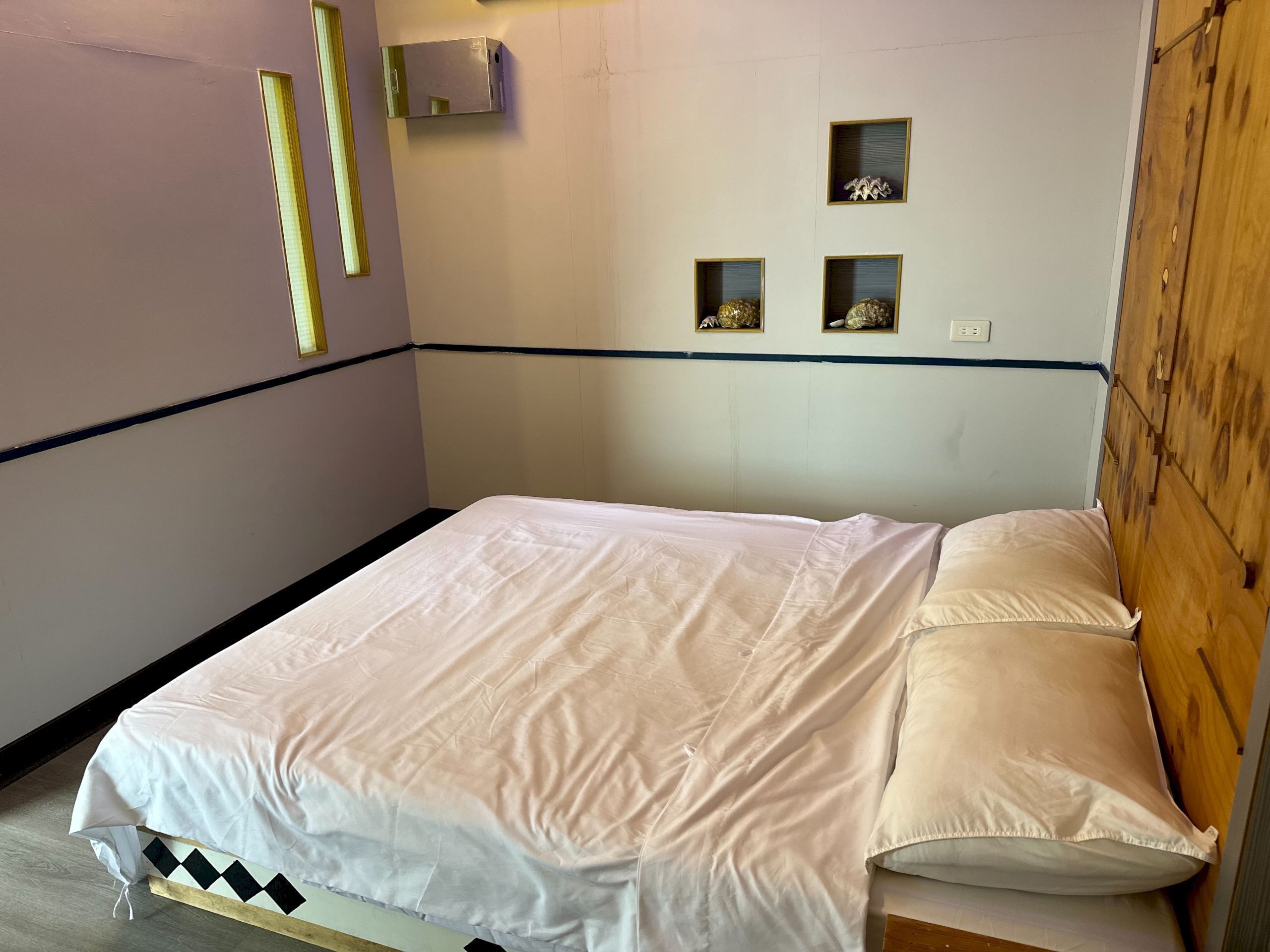 A single bed with a white mattress and matching pillow, a wooden headboard, and a wall-mounted air conditioning unit.