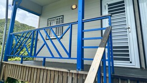Um edifício com guarda-corpo azul, uma janela com persianas brancas e uma porta com puxador de metal.