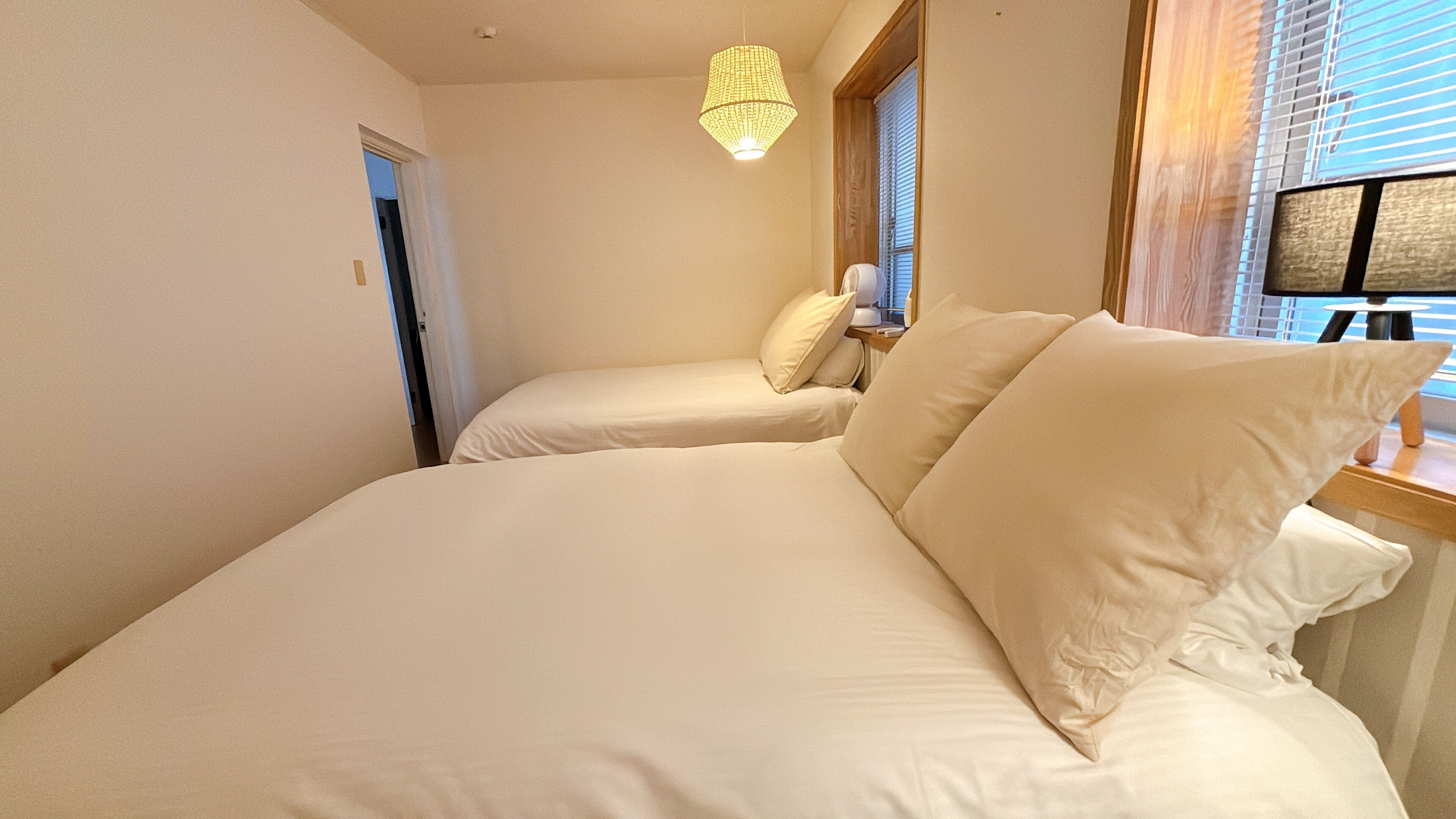 Ein Schlafzimmer mit zwei Betten, einem Fenster mit Jalousien und einer Pendelleuchte.
