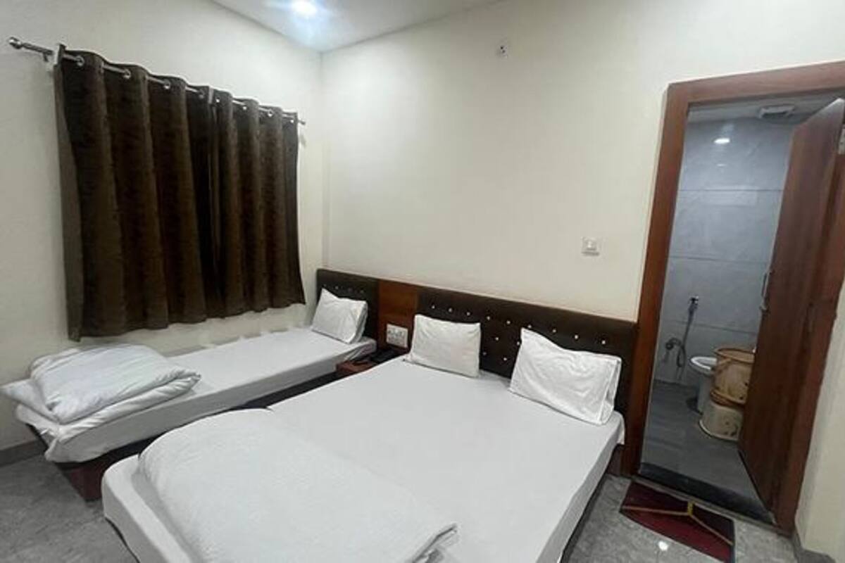 Une chambre d’hôtel avec deux lits simples, une tête de lit en bois, un rideau et une salle de bain visible à travers une porte ouverte.