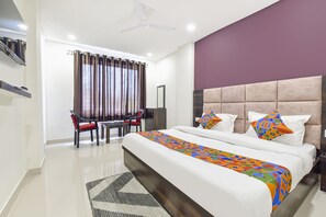 A hotel room with a large bed, a desk with two chairs, a ceiling fan, and a window with curtains. - Fabexpress Park Residency I (Haridwar)
