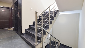A modern staircase with a metal handrail, black marble steps, and a dark door. - Fabexpress Park Residency I (Haridwar)