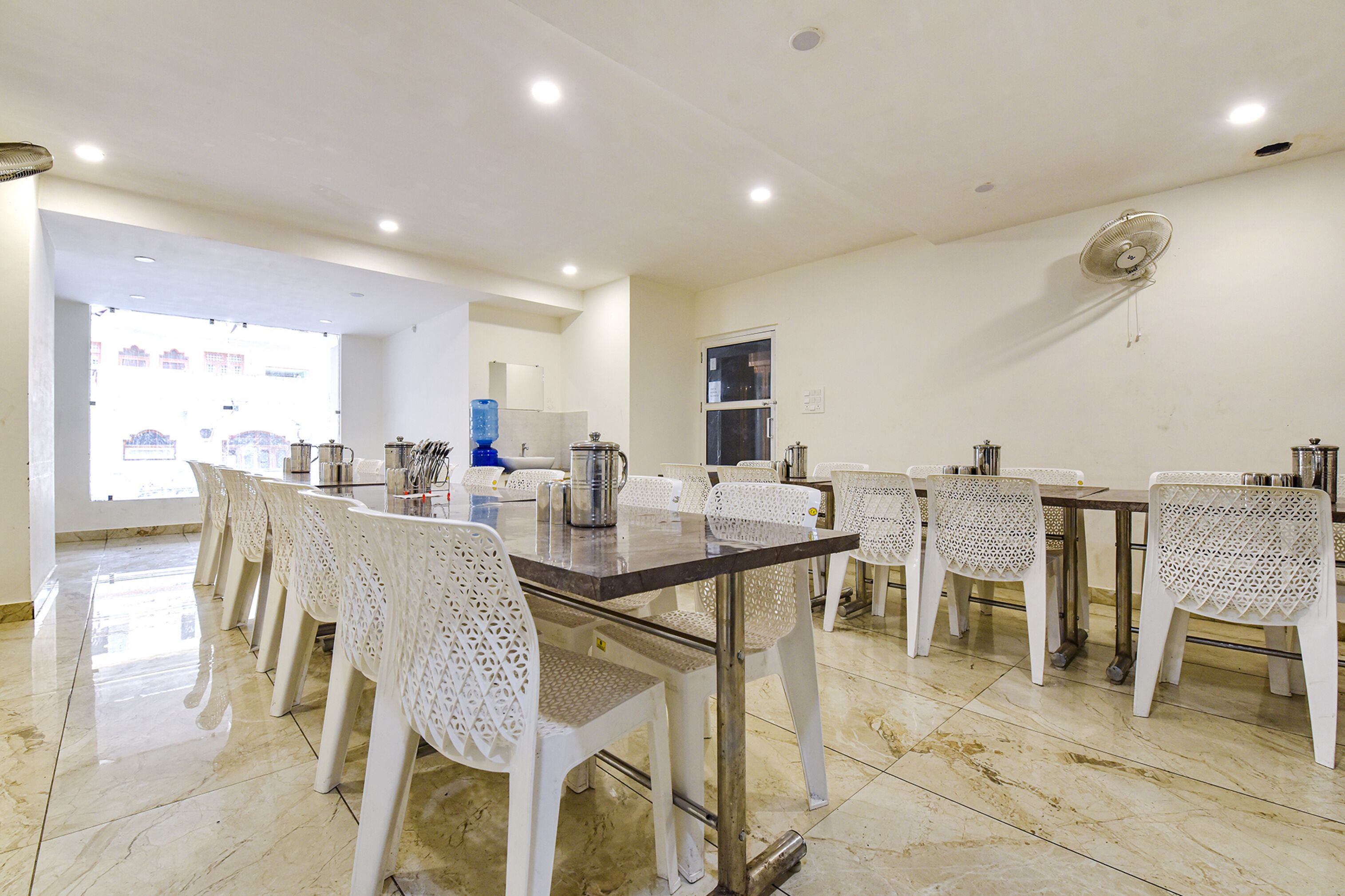 A dining area with a long table, white chairs, and a water dispenser.