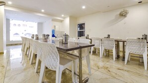 A dining area with a long table, white chairs, and a water dispenser. - Fabexpress Park Residency I (Haridwar)