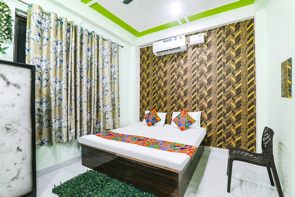 A bedroom with a bed, a chair, a green rug, and a patterned wall.
