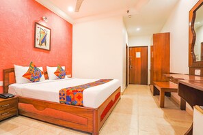 A hotel room with a wooden bed, a bedside table with a phone, a mirror, and a wooden desk. - Fabhotel Arka (Nagpur)