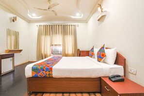 A hotel room with a bed, a desk, a chair, a ceiling fan, and a window with curtains. - Fabhotel Arka (Nagpur)