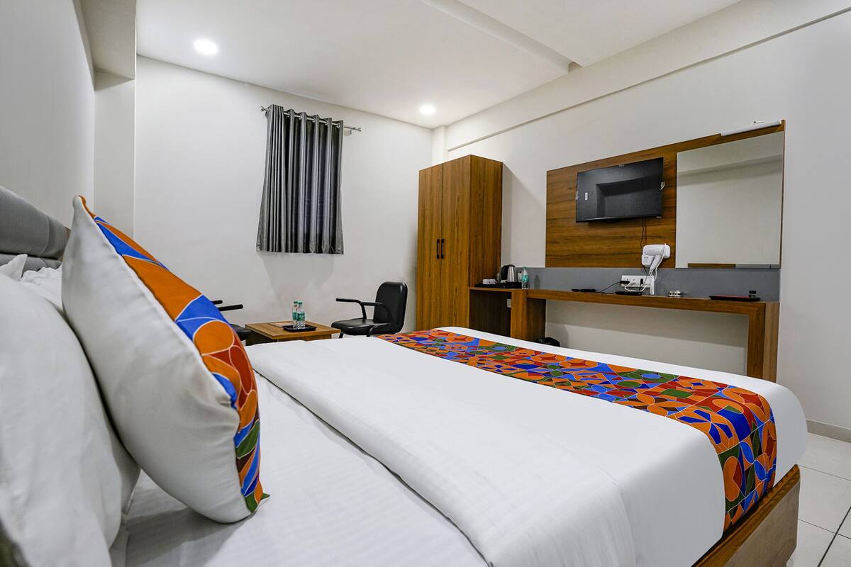 Een hotelkamer met een bed, een bureau, een stoel, een kledingkast, een televisie en een badkamer met douchegordijn.