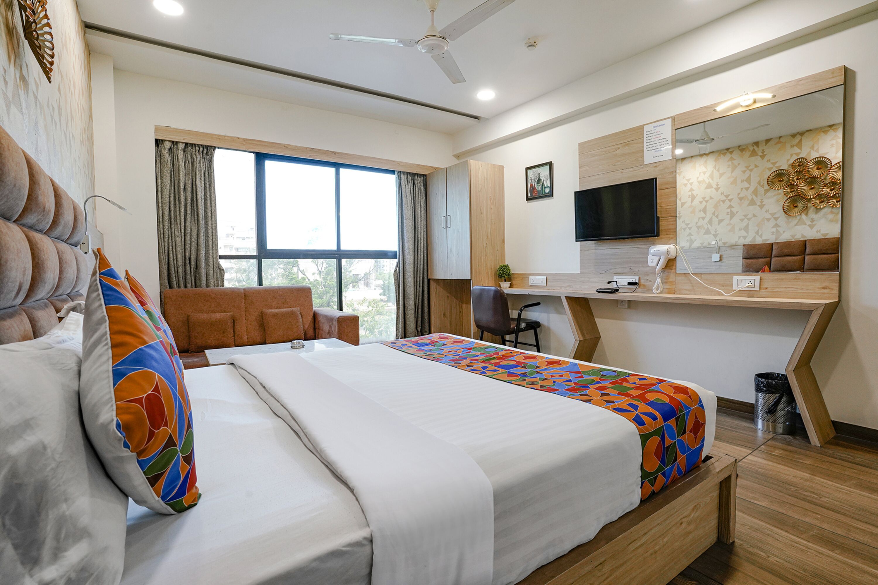 A hotel room with a bed, a desk, a chair, a television, and a window with curtains.