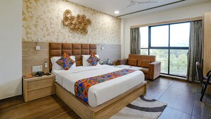 A modern hotel room with a large bed, a wooden headboard, a ceiling fan, and a view of the outdoors through a large window.