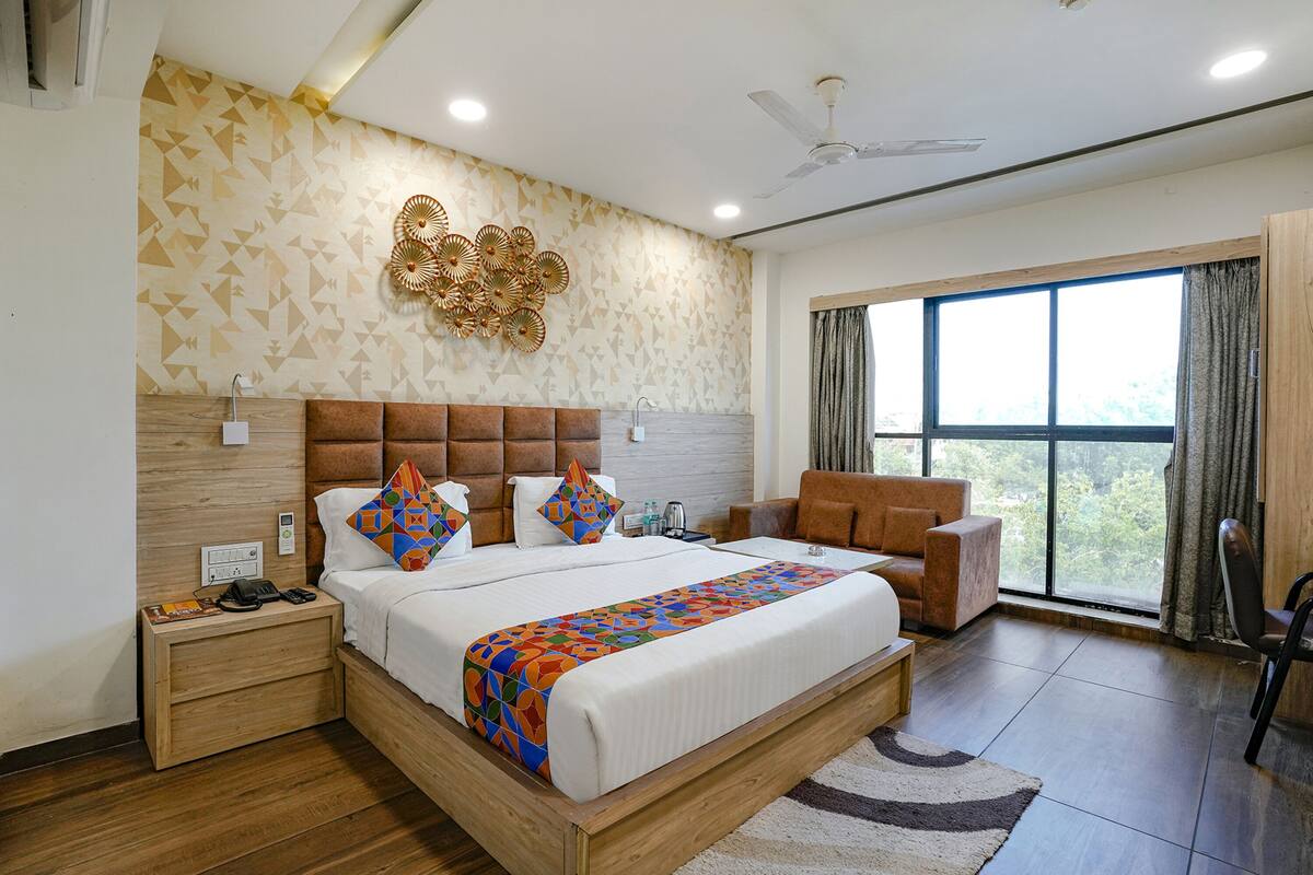 Een moderne hotelkamer met een groot bed, een houten hoofdeinde, een plafondventilator en uitzicht op het landschap door een groot raam.