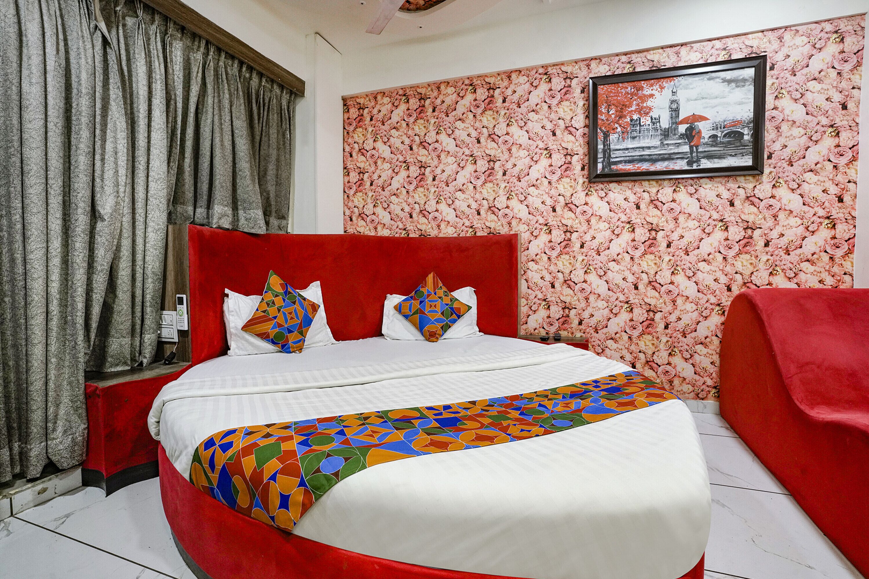 Una cama con cabecera roja, ropa de cama blanca y almohadas coloridas.