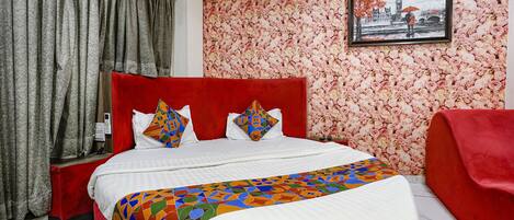 Una cama con cabecera roja, ropa de cama blanca y almohadas coloridas.