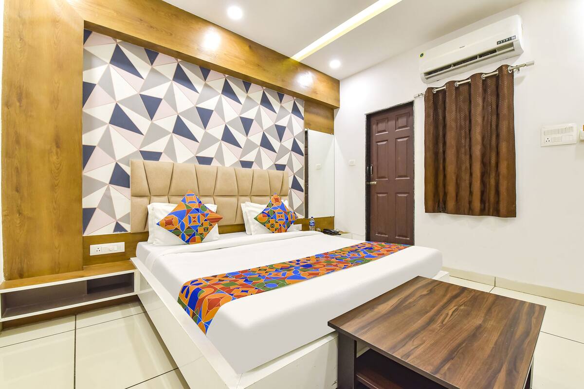 A modern hotel room with a geometric-patterned headboard, a neatly made bed with colorful bedding, a wooden nightstand, and a small wooden table.
