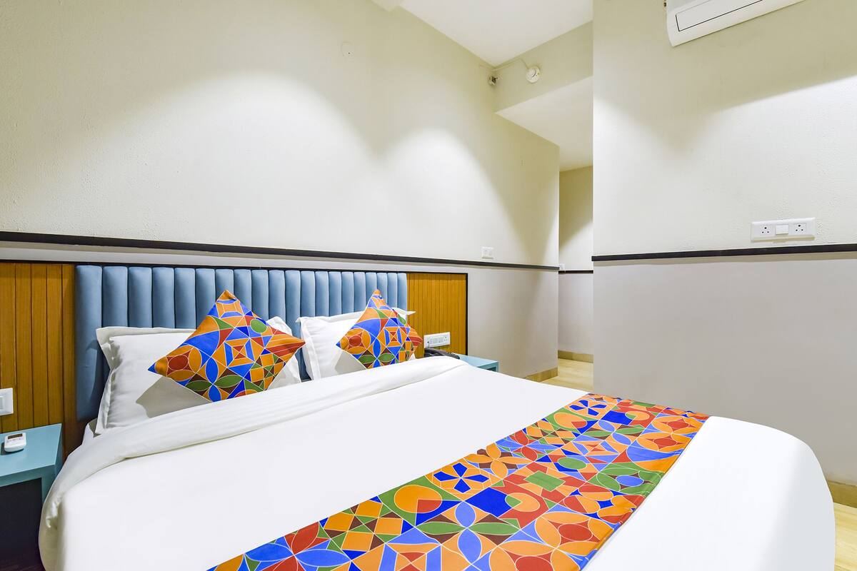A hotel room with a bed, two nightstands, a wooden headboard, and a colorful throw blanket.