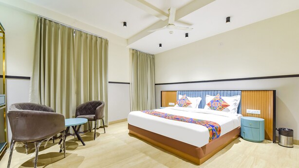 A hotel room with a large bed, two armchairs, a small table, a nightstand, and a ceiling fan. - Treebo Bella Vista (Udaipur)