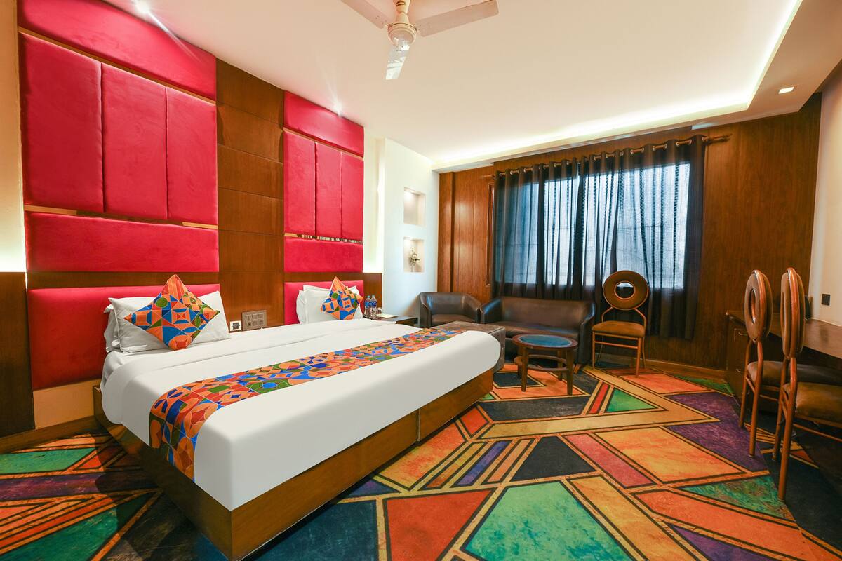 A hotel room with a large bed, a desk, a chair, a sofa, and a ceiling fan.