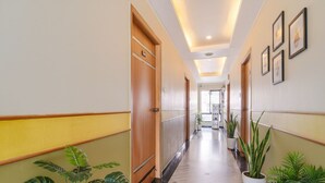 Un corridoio d'albergo con pavimento in marmo, porte in legno e piante in vaso.