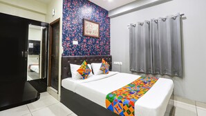A hotel room with a bed, a headboard, a mirror, a window with curtains, and a wall with a floral pattern. - FabHotel Galaxy Suites (Hyderabad)
