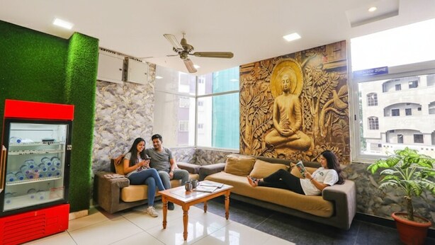 A lobby with a Buddha mural, seating areas, a red vending machine, and a ceiling fan. - FabHotel Galaxy Suites (Hyderabad)