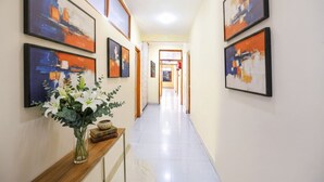 A hallway with framed abstract art on the walls, a wooden console table with a vase of flowers, and a tiled floor. - Fabhotel Grand Comforts (Srinagar)