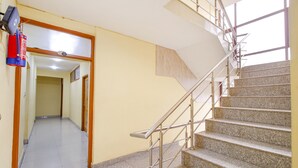 A staircase with metal railings leading to an upper floor. A fire extinguisher is mounted on the wall to the left. - Fabhotel Grand Comforts (Srinagar)