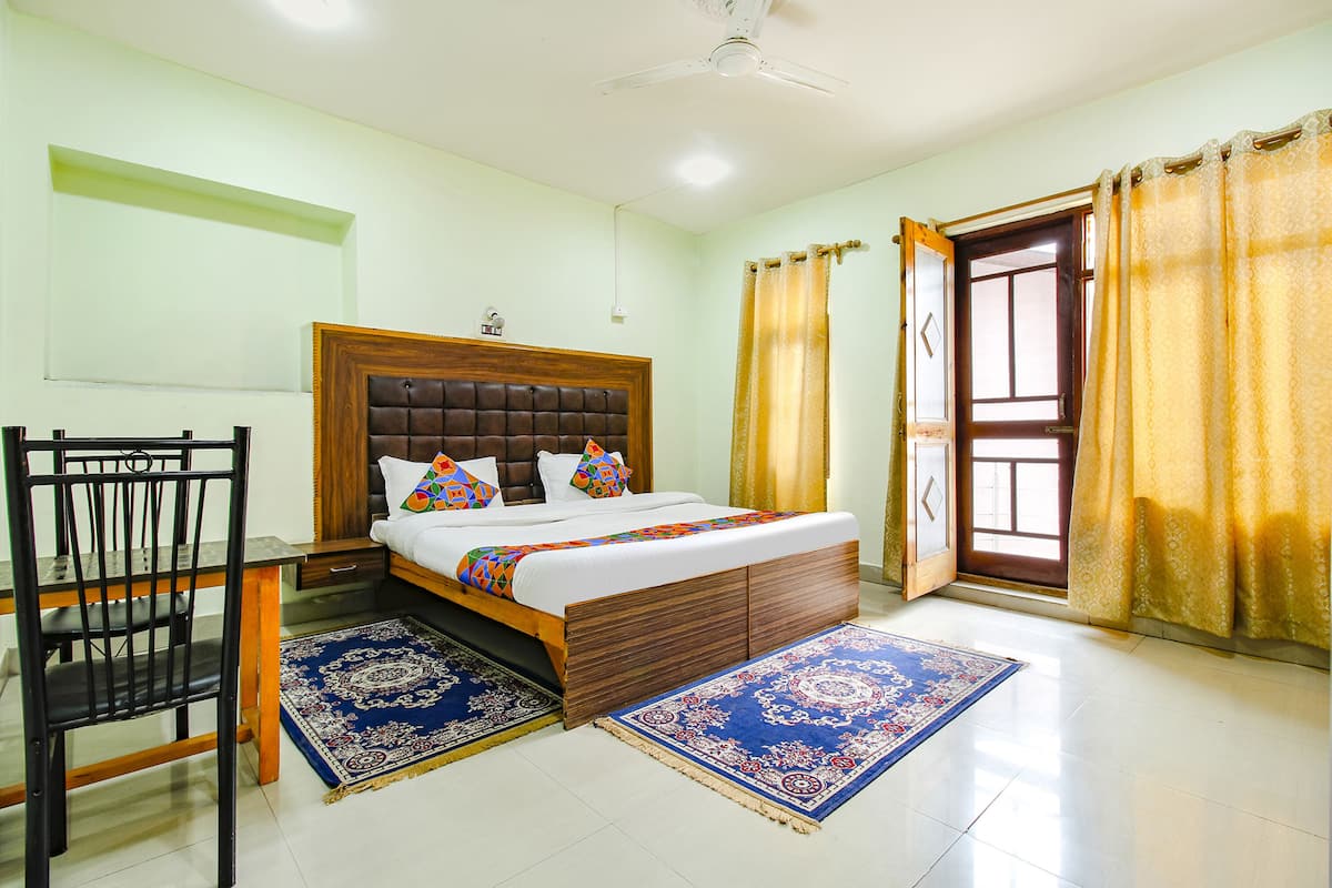 A bedroom with a bed, a desk, a chair, and a window with curtains.