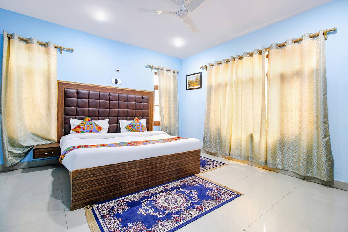A bedroom with a large bed, a headboard, curtains, a ceiling fan, and a patterned rug.