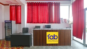Ein Empfangstresen mit einem 'fab hotels' Schild, ein Empfangsbereich und ein Fenster mit roten Vorhängen.