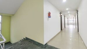 Ein langer, gut beleuchteter Flur mit einem an der Wand befestigten Feuerlöscher, einer Treppe links und Türen rechts.