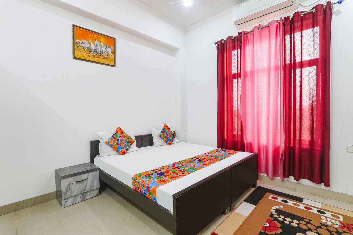 Une chambre à coucher avec un lit, une table de chevet, un rideau rouge et un tableau accroché au mur.