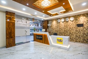 A hotel reception area with a marble floor, a reception desk labeled 'fab hotels', and a wall with clocks and a geometric pattern. - Fabhotel Heritage I (Durg)