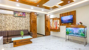 A modern lobby with a marble floor, a wooden reception desk, a brown leather sofa, a fish tank, and a TV mounted on the wall. - Fabhotel Heritage I (Durg)