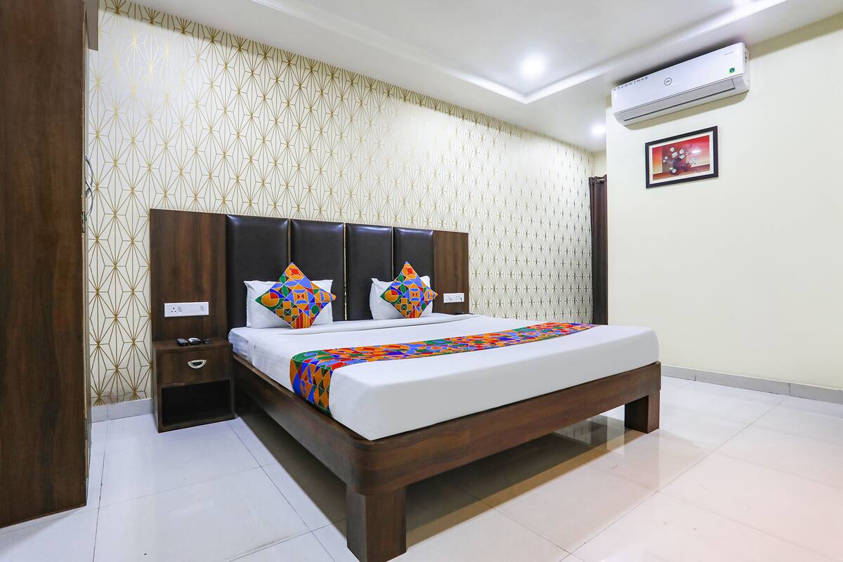 A bedroom with a wooden bed, patterned wallpaper, and a ceiling-mounted air conditioner.